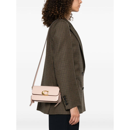 Person wearing a Coach Zoe leather shoulder bag in cream with gold-tone clasp and strap, measuring 10 cm x 19 cm x 7 cm, side view.
