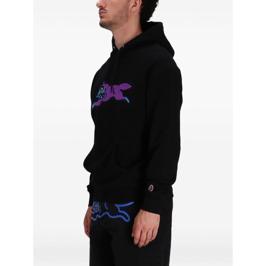 Man wearing ICECREAM Sweaters Black hoodie with dog motif and appliqué detailing.