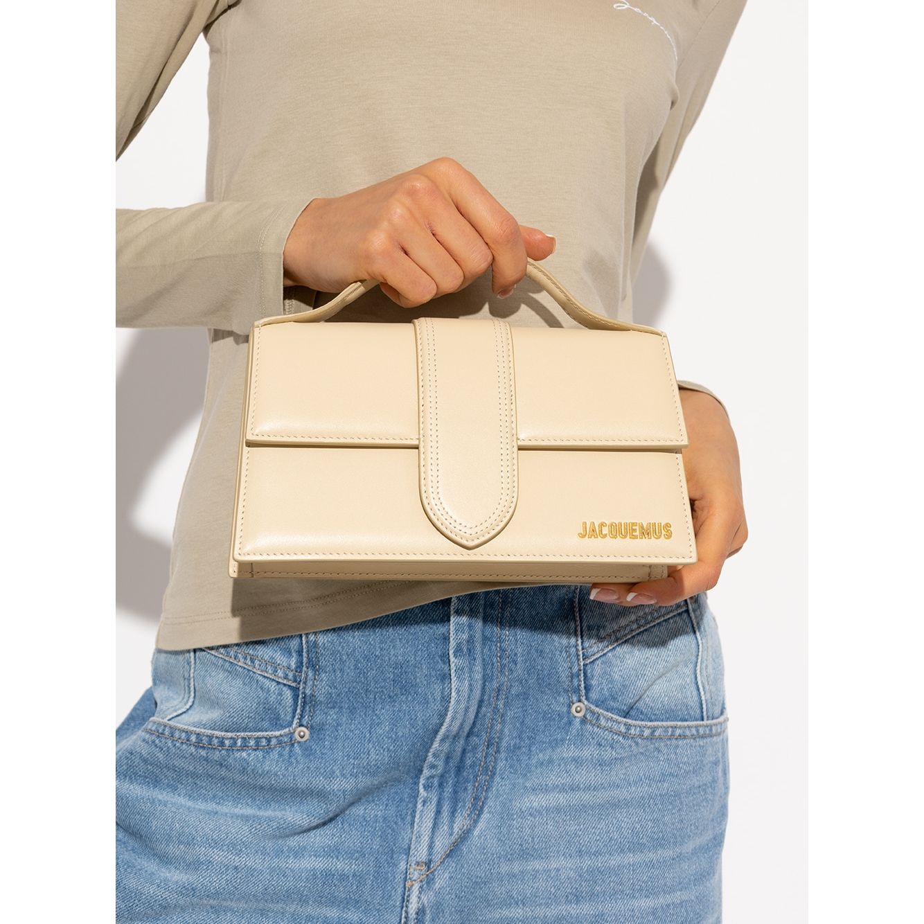 Woman holding Jacquemus Le Grand Bambino Beige Bag with gold hardware and adjustable strap.