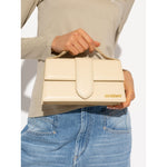 Woman holding Jacquemus Le Grand Bambino Beige Bag with gold hardware and adjustable strap.